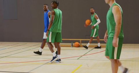 Basketball players practicing on indoor court dribbling and walking in team uniforms