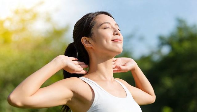 Asian woman soaking up morning sun in park breathing fresh air and smiling peacefully
