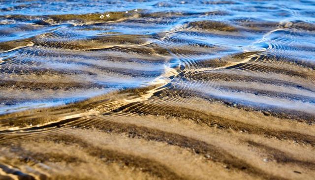 Rippling wet sand reflecting sky and sunlight in shallow tidal water, coastal texture