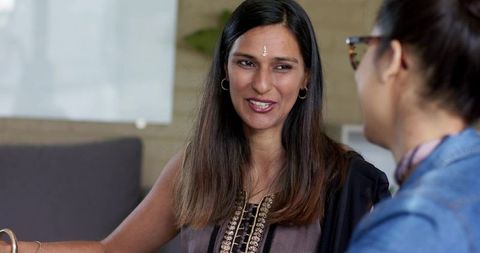 South asian woman wearing bindi and kurta smiling and talking with colleague in office