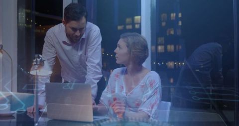 Business team collaborating late night around laptop with digital interface overlay