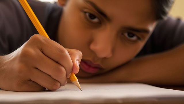 Concentrating schoolboy writing homework with sharpened pencil close-up