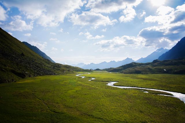 This image showcases a winding river flowing through a lush green valley surrounded by mountains under a partly cloudy sky. Perfect for use in travel brochures, nature magazines, adventure blogs, or environmental campaigns highlighting the beauty of untouched landscapes and wilderness.