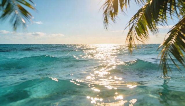 Turquoise ocean waves glinting at sunset with palm fronds framing sparkling horizon