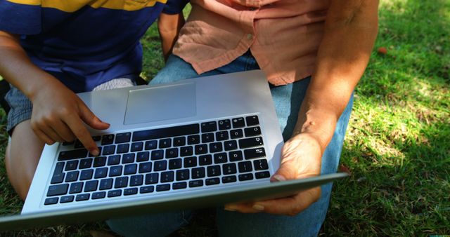 Child and adult using laptop outdoors. The hands of the adult and child are interacting with the laptop. Ideal for concepts of technology, e-learning, outdoor learning, family connection, and digital education.