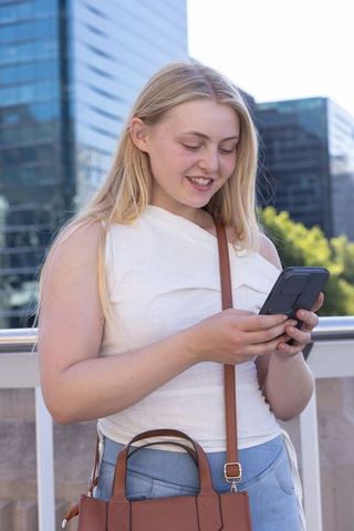 Young woman texting on smartphone while standing on urban balcony with city skyline