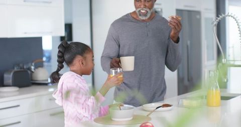 African american father daughter sharing breakfast at kitchen island enjoying orange juice