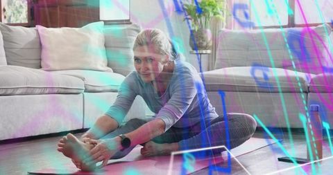 Middle-aged woman stretching on yoga mat at home with tablet and neon data overlay