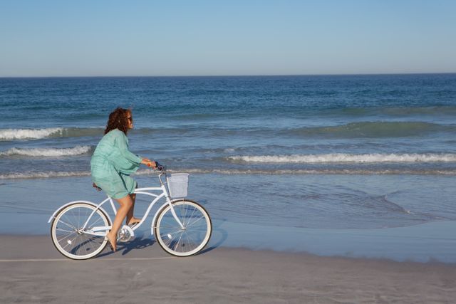 Side view of biracial woman riding bicycle on beach in the sunshine