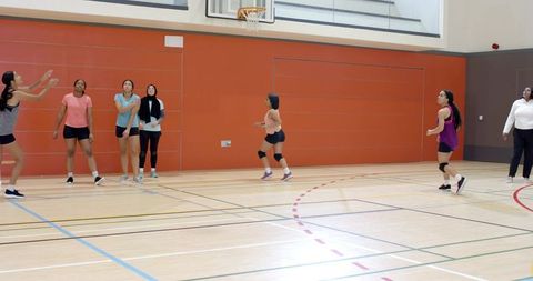 Female athletes practicing team drill under basketball hoop inside school gymnasium