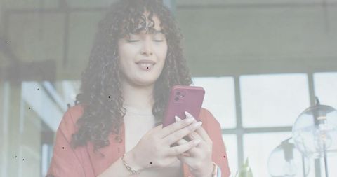 Young woman using magenta smartphone syncing apps with laptop in modern coworking space