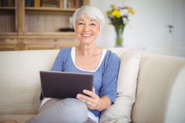 Smiling senior woman using digital tablet in living room - Download Free Stock Photos Pikwizard.com