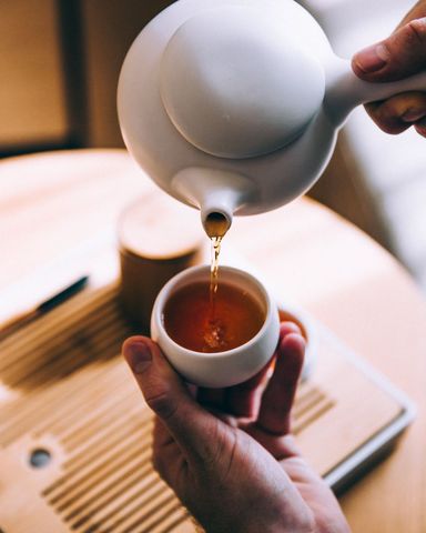 Pouring Tea into Cup with Ceramic Teapot on Wooden Table