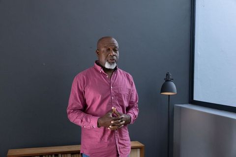 Senior man in magenta shirt standing in minimalist grey room