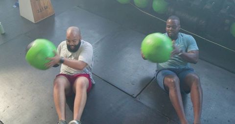 African men performing partner medicine ball core workout in gym for strength, team fitness