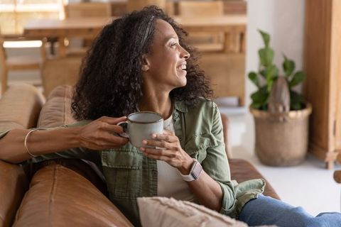Relaxing woman reclining on leather couch sipping coffee in cozy modern living room