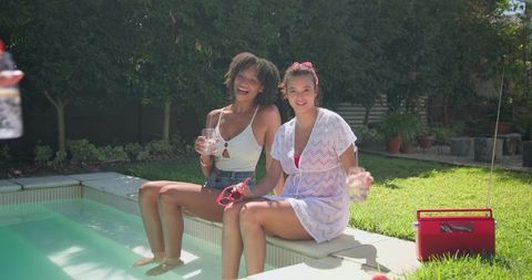 Joyful friends relaxing poolside with refreshing drinks