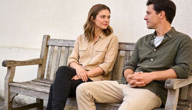 Couple sharing quiet conversation on weathered wooden bench in sunny courtyard