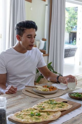 African american man reaching for glass at sunlit dining table with curry, rice and naan