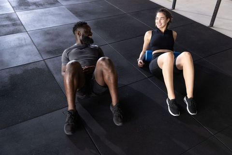 Couple doing post-workout foam rolling on gym rubber floor smiling together