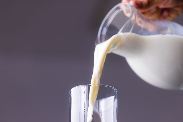 Cropped hand pouring milk in glass against gray background, copy space. unaltered, food, drink, studio shot and healthy eating.