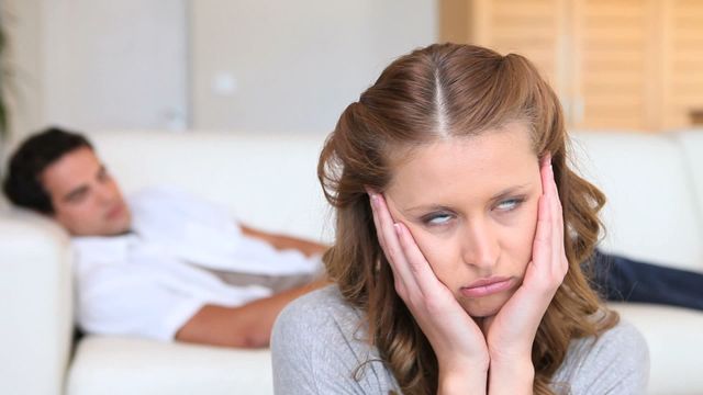 This image captures a woman expressing boredom and frustration while her partner sleeps in the background. It is suitable for illustrating topics related to relationship issues, silent conflicts, or emotional disconnects in couples. Might be used for blog posts, articles, or advertisements focused on relationship advice or interpersonal dynamics.