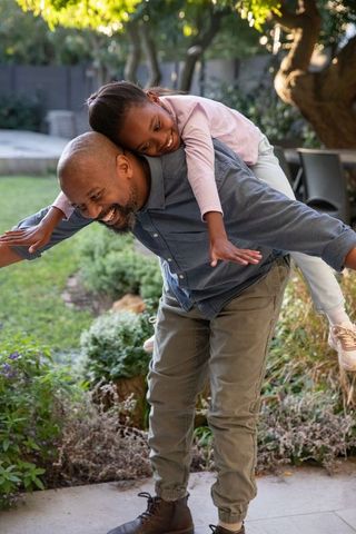 African american father giving piggyback ride to smiling daughter in sunlit backyard