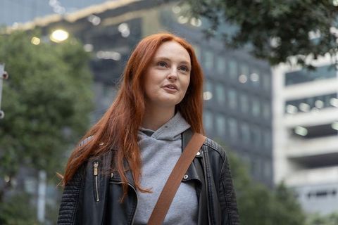 Redhead woman gazing upward on urban street wearing gray hoodie and leather jacket