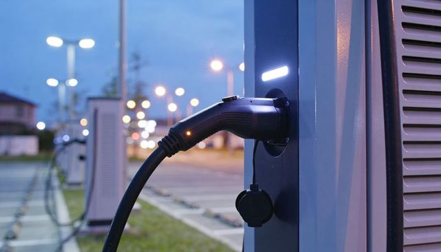 Plugging ev charging connector into public charging station at dusk with led glow