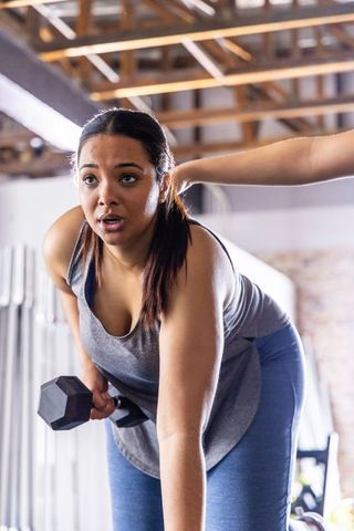 African american woman performing single-arm dumbbell row while trainer coaching in gym