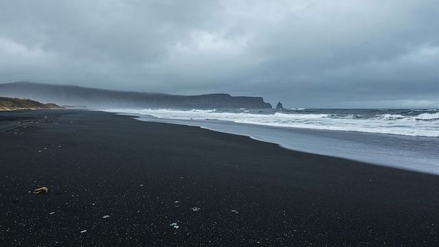 Majestic Black Sand Beach with Rolling Waves and Distant Cliffs