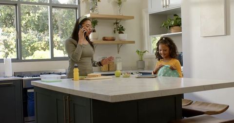 Busy mom multitasking on phone while child packing lunch at modern marble kitchen island