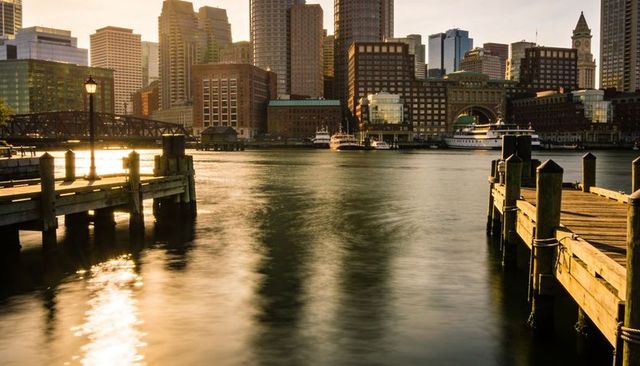 Golden-hour waterfront framing downtown skyline between wooden piers with ferry reflections