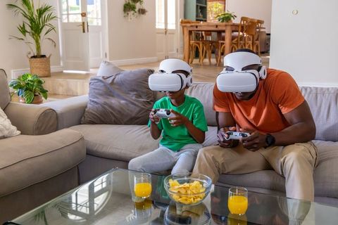 African American father and son playing VR together on couch with white headsets