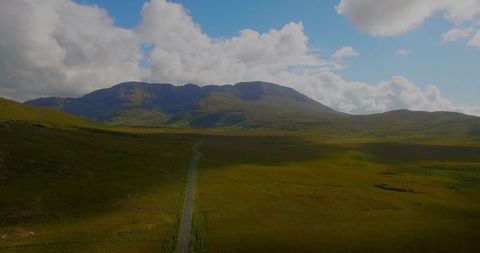 Narrow Road Through Countryside Leading to Majestic Mountains