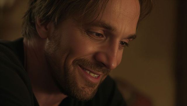 Smiling man showing dimples and skin texture in warm amber closeup portrait, intimate