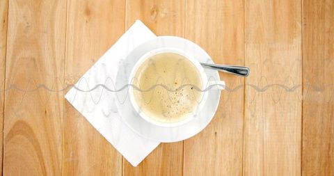 Savoring morning coffee on rustic wooden tabletop with white ceramic cup, foam, spoon