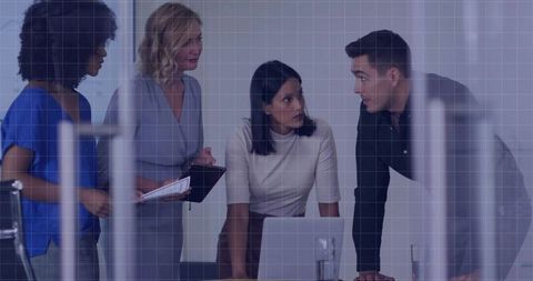 Team collaborating around laptop in glass conference room with manager leaning in
