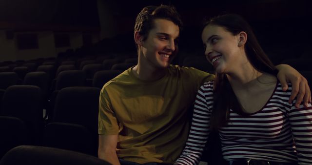Happy teenage girlfriend and boyfriend sitting in dark theatre eat embracing and smiling, copy space. Theatre, romance, adolescence and love, unaltered.