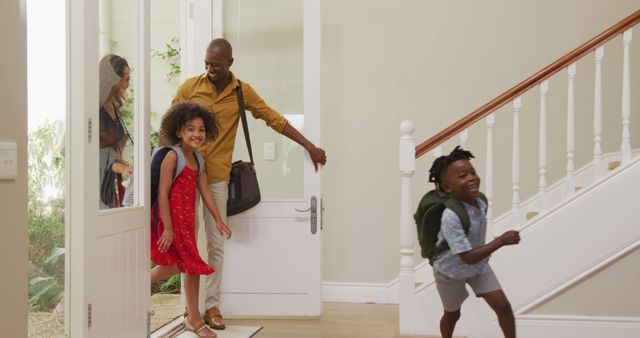 A happy family is entering their home with excitement. The parents, carrying bags, are smiling while the children, wearing backpacks, are rushing inside energetically. This image highlights familial joy and togetherness. Perfect for use in advertisements promoting family life, home-buying services, moving services, and educational materials about family dynamics.
