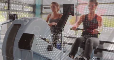 Women Training on Rowing Machine with Digital Monitoring at Fitness Studio