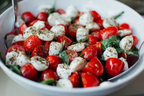 Serving cherry tomato mozzarella caprese salad with fresh basil and oregano