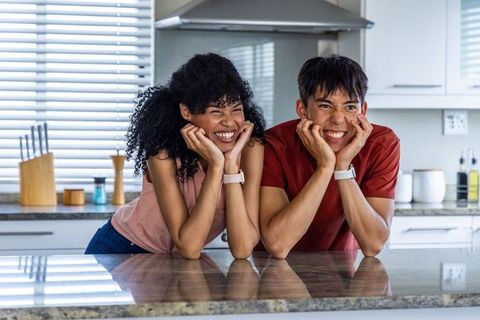 Young couple leaning on kitchen island smiling and wearing smartwatches, modern home warmth
