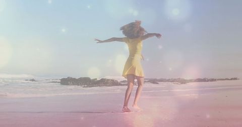 Carefree woman spinning on sunlit beach in yellow dress