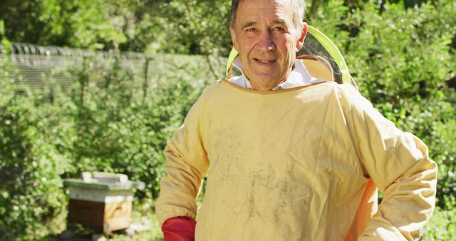 Senior beekeeper in protective gear stands proudly in a garden apiary. Perfect for depicting hobbies, retirement activities, sustainable living, and small-scale farming projects.
