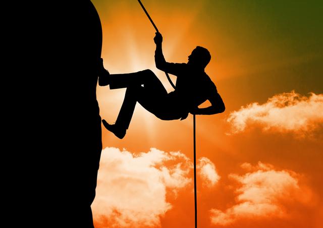 Man scaling mountain with rope silhouetted against vibrant sunset sky, evoking themes of adventure and determination. Ideal for use in outdoor sports advertisements, motivational posters, and adventure tourism promotions.