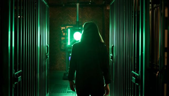 Walking woman approaching circular neon green light between industrial metal doors