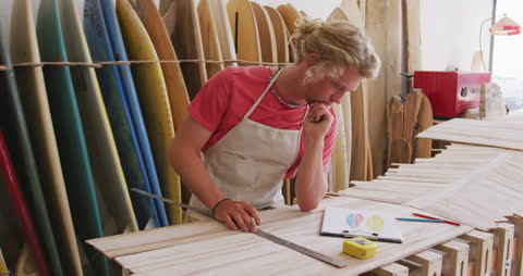 Surfboard Maker Measuring Materials in Workshop with Surfboards in Background