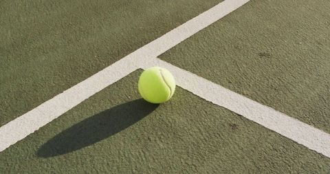 Tennis ball resting on hardcourt casting dramatic long shadow across white lines