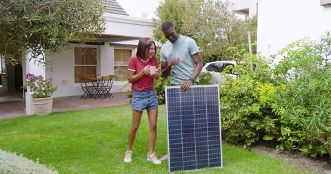Diverse Couple with Solar Panel on Suburban Lawn Exploring Eco-Friendly Living